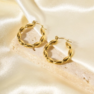 Dettaglio di orecchini a cerchio in oro 18K testurizzati su pietra e seta elegante