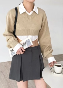 Detail of layered beige V-neck knit sweater over white collared shirt with pleated skirt
