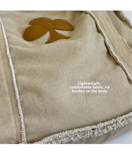 Detail view of canvas tote bag featuring raw fringe edges and brown leather floral patch
