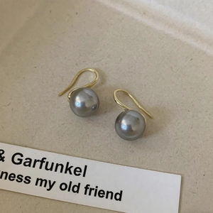 Detail of 18K gold hook earrings with round grey pearl on a beige display tray