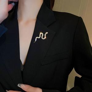 Detailed close-up of a gold-plated snake brooch with cubic zirconia on a black blazer