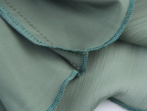 Makro-Detail von salbeigrünem Chiffon-Stoff und professioneller Overlock-Nahtverarbeitung