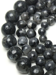 Macro shot of natural dark grey labradorite beads on white silk with detailed stone texture