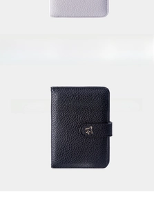 Close-up of black lychee grain leather passport holder with golden airplane buckle detail