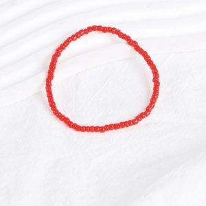 Close-up of a vibrant red beaded bracelet with small round beads on a white textured surface