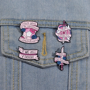 Close-up of four pink enamel pins with motivational quotes on a denim jacket pocket