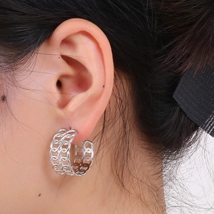 Close-up of silver hollowed pattern earring worn on ear with metallic luster finish