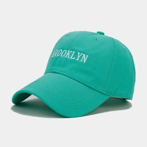 Detailed close-up of white Brooklyn embroidery on a teal blue cotton baseball cap