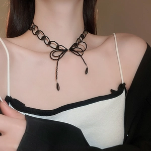 Close-up of black beaded necklace featuring a bow pendant and dangling tassels on model