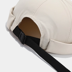 Detail of beige docker hat showing adjustable black strap and buckle with twill texture