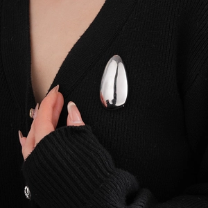 Close-up of polished silver irregular oval brooch on a black knitted cardigan