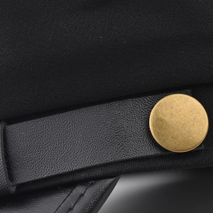 Detail of black PU leather band and vintage gold button on a stylish flat top cap