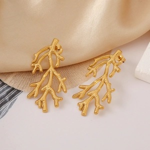 Close-up of gold coral branch earrings on soft beige silk fabric with metallic luster