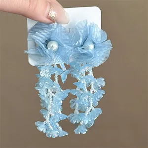 Close-up of blue fabric flower earrings with white beaded tassels and faux pearl center