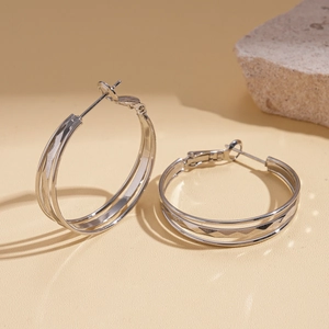 Macro detail of silver layered hoop earrings with hammered texture on sand background