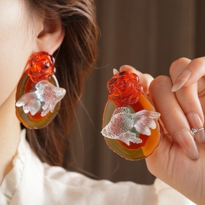 Macro detail of amber resin earrings with red roses and transparent goldfish charms