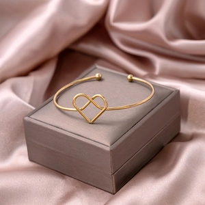 Detailed view of an open gold heart bracelet with beads on a satin jewelry display