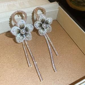 Détail de boucles d'oreilles brodées en fleur avec perle et glands en strass