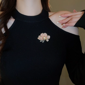 Detailed close-up of a pink floral brooch with gold edges and pearl on a black sweater