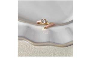 Detail of adjustable gold ring with pink enamel and a pear-cut zircon on ceramic tray