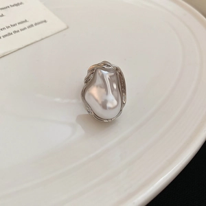Makro-Detail eines Barockperlenrings mit unregelmäßigem Silberrahmen auf einem Keramikteller