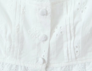 Détail de broderie anglaise blanche en coton avec des boutons recouverts de tissu fin