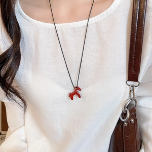 Gros plan d'un collier pendentif poney rouge avec cordon noir sur un pull blanc
