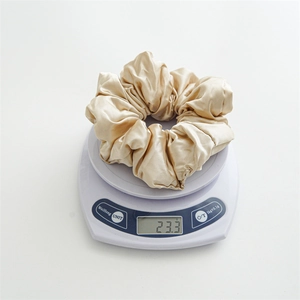 Detailed shot of large champagne gold satin scrunchie weighing 23.3g on a digital scale