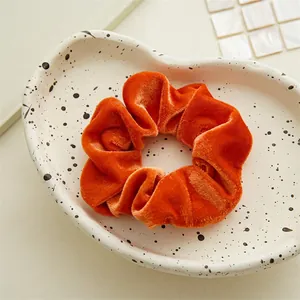 Detailed view of an orange velvet scrunchie with soft ruffled texture and satin sheen