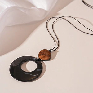 Detail of minimalist long necklace featuring resin and wood ring pendant on beige surface