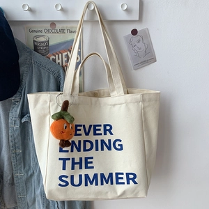 Close-up of beige canvas tote bag with blue summer typography and orange charm