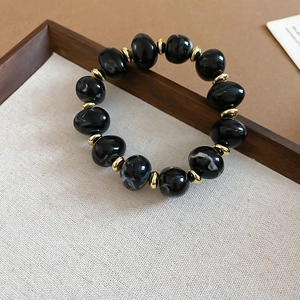 Detail of beaded bracelet featuring black marbled acrylic beads and gold metal spacers
