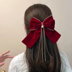 Dettaglio del fermaglio a fiocco in velluto rosso con perla e nappe di strass su modella