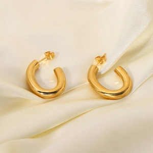 Gros plan de boucles d'oreilles en C dorées sur soie blanche montrant le placage 18 carats