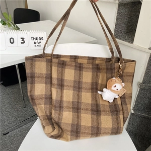 Close-up of brown plaid tote bag texture and cute cat plush pendant on white chair