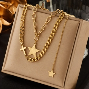 Layered gold necklace featuring cross and smiley star pendants on a beige display