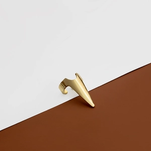 Bague d'armure dorée à griffes au design pointu sur un fond bicolore minimaliste