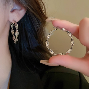 Detailed view of twisted circular earrings with silver pins and metallic textured finish