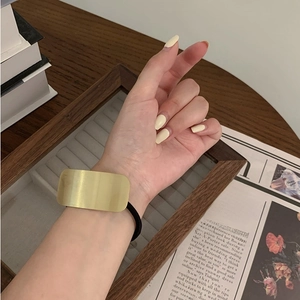 Close-up of a minimalist gold rectangular metal plate hair tie on a black elastic band