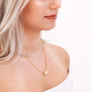 Dettaglio di una collana dorata con ciondolo lettera A e cuore indossata da una donna