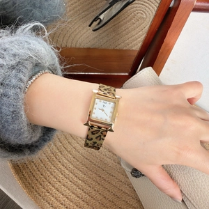 Close-up of golden H-shaped square watch with leopard print mesh strap on a female wrist