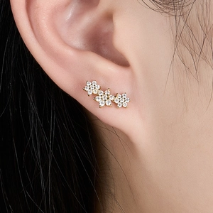 Close-up of sparkling gold flower earrings with inlaid cubic zirconia on a model's ear