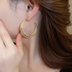 Detailed shot of large gold-plated crescent hoop earrings with purple and white zircons