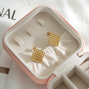 Elegant gold square stud earrings with bead texture on pink jewelry organizer