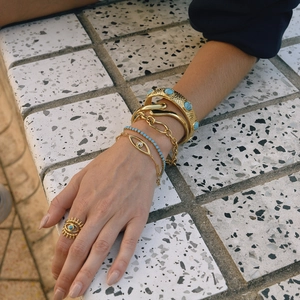 Detail view of gold layered bracelets and rings with turquoise evil eye motifs