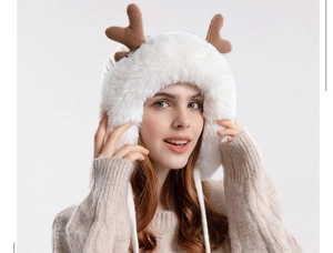 Close-up of white plush earflap hat with brown antlers and decorative pom-poms