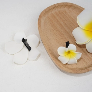Detail of plumeria flower hair clips with white petals and yellow center on wooden tray