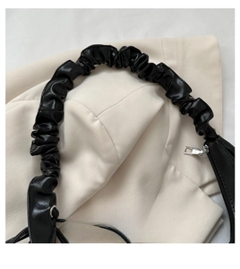 Detail of black shoulder bag featuring ruched scrunchie handle and silver hardware accent