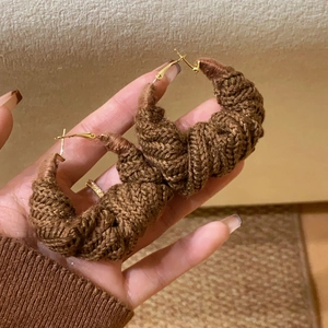 Detailed view of hand-held brown knitted circular earrings with woven wool texture