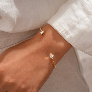 Detail eines minimalistischen goldenen C-Armreifs mit Zirkonia auf Leinenhintergrund
